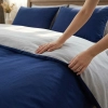 Zbliżenie dłoni odkrywającej drugą stronę pościeli J&W, widoczny kontrast granatu i jasnej szarości.