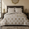 Stylowa sypialnia w ciepłych kolorach z bogato zaścielonym łóżkiem ubranym w geometryczną pościel (wzór Marokańska Koniczyna).