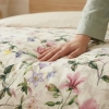 Zbliżenie dłoni na miękki materiał pościeli z malarskim wzorem kwiatów wiśni