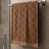 Karmelowo-brązowy, miękki ręcznik frotte Fiamo o wymiarach 50x100 cm z grubym, tłoczonym wzorem, powieszony na wieszaku pod prysznicem.