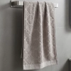 Jasnobeżowy (kremowy) ręcznik do rąk i twarzy z kolekcji Fiamo 50x100 w elegancki wzór, powieszony na wieszaku w jasnej łazience.