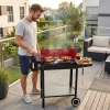 Mężczyzna przygotowujący posiłek na ogrodowym grillu węglowym z kółkami