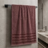 Ręcznik frotte Mondo w odcieniu zgaszonego bordo z elegancką pasiastą bordiurą, wiszący na czarnym, matowym relingu.
