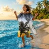 Radosna kobieta biegnąca w morskich falach, mająca na sobie plażowe poncho z kapturem i egzotycznym motywem palm
