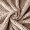 Tekstura miękkiej mikrofibry jasnobrązowego szlafroka ułożona w przestrzenną falę ukazująca gęstość materiału