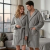 Uśmiechnięta para w sypialni ubrana w grube jasnoszare szlafroki kąpielowe z kapturem z miękkiej mikrofibry