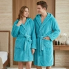 Uśmiechnięta para w sypialni ubrana w grube turkusowe szlafroki kąpielowe z kapturem z miękkiej mikrofibry