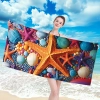 Uśmiechnięta kobieta w bikini trzymająca poziomo rozłożony duży ręcznik plażowy z mikrofibry w wielokolorowe morskie roz