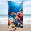 Pionowa prezentacja dużego ręcznika plażowego we wzór oceanu i uroczych rybek, trzymanego przez osobę stojącą na piaszczystej plaży