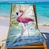 Lekki ręcznik plażowy z flamingiem i kwiatowymi wzorami zawieszony na leżaku na rajskiej plaży z jasnym piaskiem.
