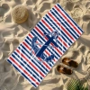 Lekki ręcznik plażowy w paski z kotwicą leżący na piaszczystej plaży obok słomkowego kapelusza, klapków i liścia palmy.