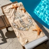 Ogromny ręcznik plażowy XXL z motywem kotwicy z muszli i rozgwiazd ułożonych na piasku, na leżaku przy basenie