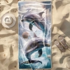 Duży ręcznik plażowy XXL z mikrofibry ze wzorem skaczących delfinów i muszli, rozłożony na piasku obok kapelusza - TwójD