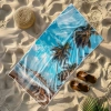 Wielki ręcznik plażowy Serena z fotorealistycznym krajobrazem morza i piasku, leżący obok słomkowego kapelusza