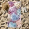 Odporny na piasek ręcznik z mikrofibry o wzorze pastelowych serc leżący obok kapelusza i białych klapek na plaży