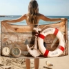 Kobieta na plaży trzyma za plecami ręcznik z kołem ratunkowym i kompasem na tle drewna - TwójDomNa5.pl