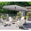 Duży parasol Solano (350 cm) w kolorze jasnoszarym z dekoracyjną falbaną, rzucający przyjemny cień na białe krzesła wypoczynkowe na tarasie, w otoczeniu zieleni.