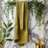 Elegancki, oliwkowozielony ręcznik łazienkowy Rimini z bawełny zawieszony na złotym relingu w designerskim wnętrzu.