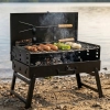 Rozłożony czarny grill przenośny węglowy na kamienistej plaży. Mały grill turystyczny z rusztem, na którym pieką się kiełbaski i szaszłyki podczas plenerowego BBQ