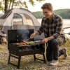 Składany grill kempingowy węglowy w użyciu nad jeziorem. Mężczyzna przygotowujący posiłek na kompaktowym grillu turystycznym obok namiotu na biwaku.