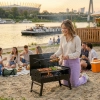 Piknik ze znajomymi i mały grill węglowy na piaszczystej plaży. Kobieta piekąca szaszłyki na przenośnym grillu turystycznym podczas plenerowej imprezy.