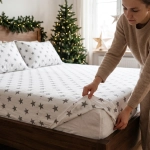 Białe świąteczne prześcieradło tradycyjne bez gumki z bawełny premium we wzór dużych szarych gwiazdek ułożone na łóżku w