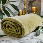 Puszysty ręcznik frotte do twarzy 50x100 w kolorze oliwkowym, ułożony w kostkę na jasnym marmurze w otoczeniu zieleni.