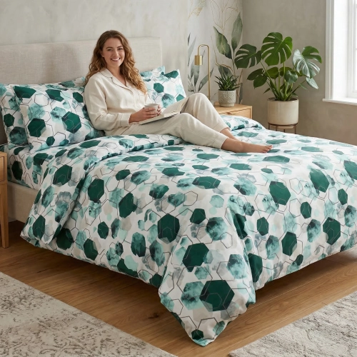 Uśmiechnięta kobieta w jasnej piżamie siedzi na łóżku z nowoczesną, geometryczną pościelą z bawełny premium J&W.