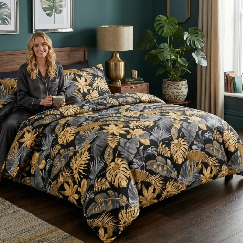 Uśmiechnięta kobieta w eleganckiej piżamie siedzi na łóżku z luksusową, tropikalną pościelą z bawełny premium J&W w złot