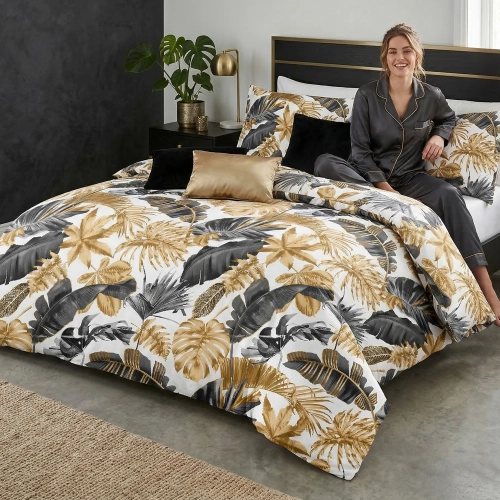 Uśmiechnięta kobieta w szarej satynowej piżamie relaksuje się na łóżku z elegancką, tropikalną pościelą z bawełny premiu