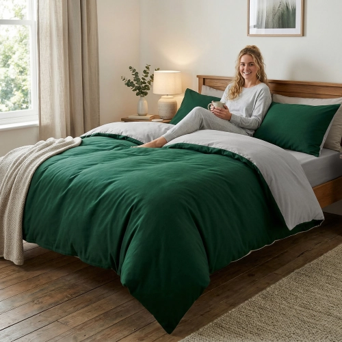 Kobieta relaksuje się na łóżku z dwustronną pościelą J&W w kolorach butelkowej zieleni i jasnej szarości.