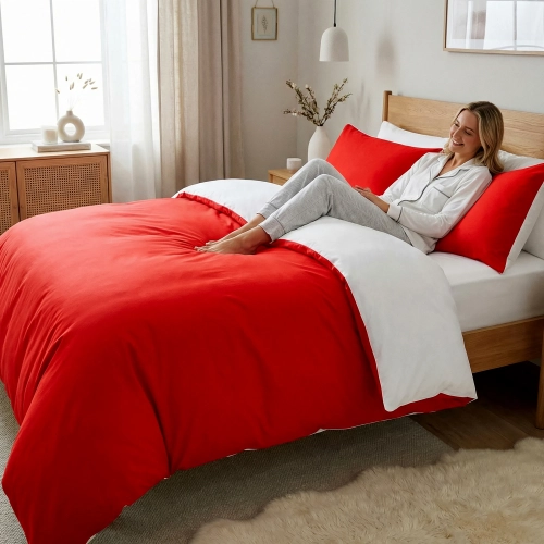 Uśmiechnięta kobieta relaksuje się w łóżku z dwustronną, czerwono-białą pościelą J&W.