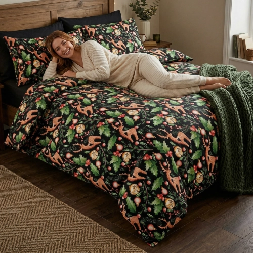 Uśmiechnięta kobieta leży na łóżku zaścielonym elegancką pościelą z bawełny J&W we wzór zimowych reniferów na czarnym tl