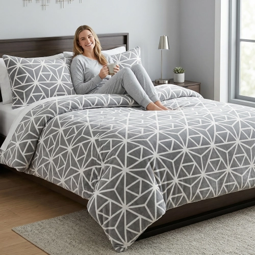 Kobieta relaksująca się na łóżku z szarą, wygodną pościelą bawełnianą J&W we wzór geometrycznych linii.