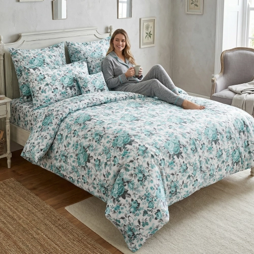 Kobieta relaksująca się na łóżku z białą, wygodną pościelą bawełnianą J&W we wzór chłodnych róż.