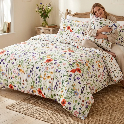 Uśmiechnięta kobieta przytula poduszkę, siedząc na łóżku zaścielonym jasną pościelą z bawełny premium J&W w polne kwiaty