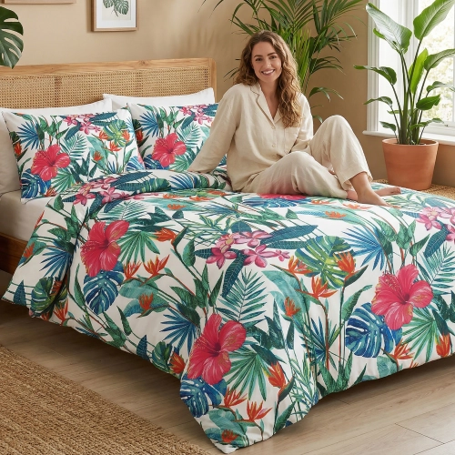 Kobieta w jasnej piżamie z uśmiechem relaksuje się na łóżku zaścielonym elegancką, letnią pościelą z egzotycznym motywem