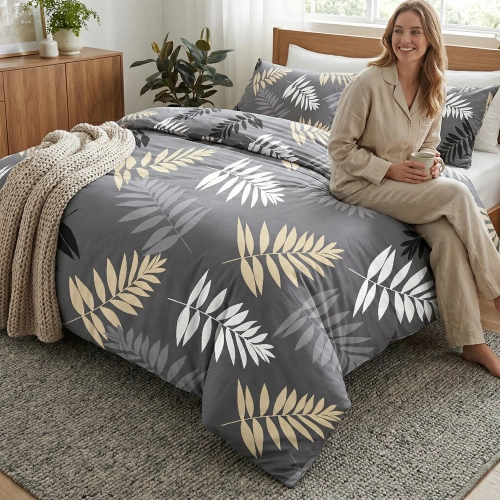 Uśmiechnięta kobieta w jasnej piżamie siedzi z kubkiem na łóżku z grafitową pościelą z bawełny premium J&W we wzór jasny