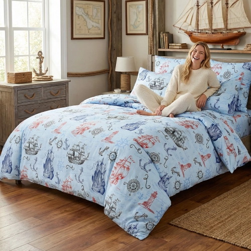 Łóżko zaścielone elegancką pościelą z bawełny J&W we wzór statków w marynistycznych barwach, w jasnej sypialni.