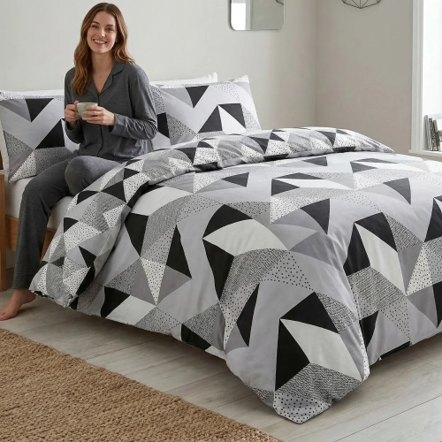 Kobieta w ciemnoszarej piżamie prezentująca z uśmiechem na łóżku stylową pościel w duże, geometryczne trójkąty od J&W.