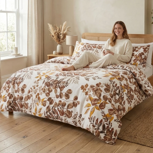 Uśmiechnięta dziewczyna siedzi na łóżku z piękną, botaniczną pościelą J&W we wzór ciepłych, jesiennych liści.