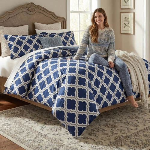 Łóżko zaścielone elegancką pościelą z bawełny J&W we wzór jasnej koniczyny na granacie, w sypialni.