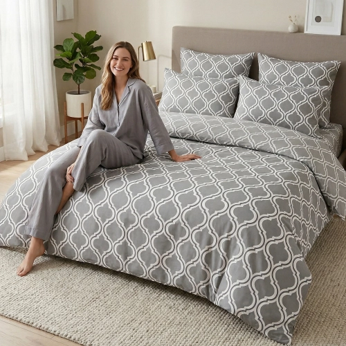 Kobieta w szarej piżamie z uśmiechem odpoczywa na łóżku z bawełnianą pościelą J&W we wzór popielatej koniczyny marokańsk