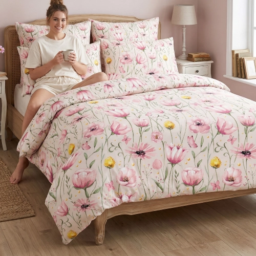 Kobieta relaksująca się na łóżku z kubkiem, zaścielonym w wygodną pościel bawełnianą J&W we wzór różowych kwiatów.