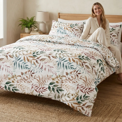 Kobieta relaksująca się z uśmiechem na łóżku zaścielonym w wygodną pościel bawełnianą J&W we wzór jesiennych liści.