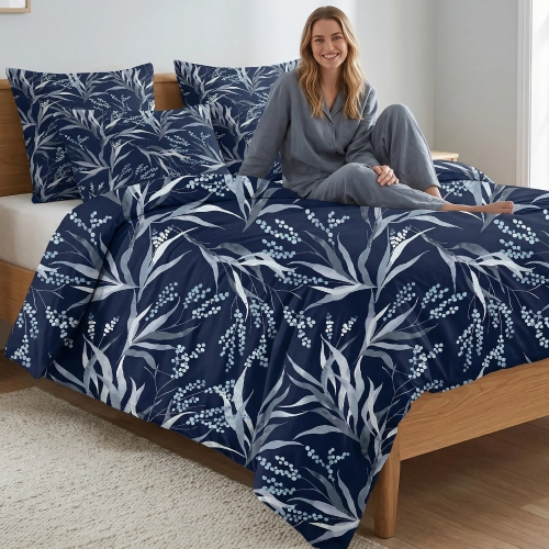 Kobieta w szarej piżamie relaksuje się na łóżku z luksusową, granatową pościelą z bawełny J&W z motywem jasnych liści.