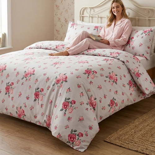 Kobieta w różowej piżamie relaksuje się z książką na dużym łóżku, zaścielonym w białą, bawełnianą pościel J&W w malinowe