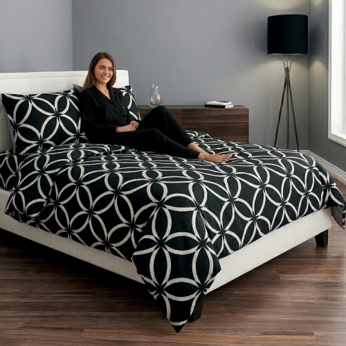 Kobieta relaksująca się na łóżku z czarną, wygodną pościelą bawełnianą J&W we wzór białej marokańskiej koniczyny.