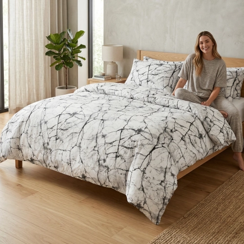 Kobieta relaksująca się na łóżku z białą, wygodną pościelą bawełnianą J&W we wzór żyłek ciemnego marmuru.