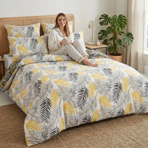 Kobieta w piżamie z uśmiechem relaksuje się na łóżku z białą pościelą J&W we wzór musztardowych i czarnych liści palmy.